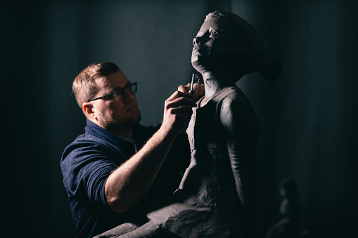 Man sculptor creates sculpt bust clay human woman sculpture. Statue craft creation workshop