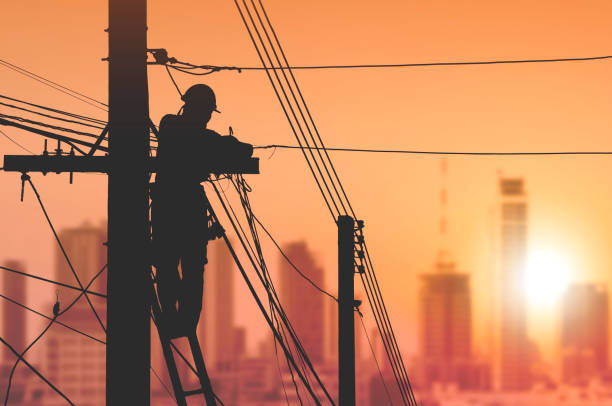Silhouette electrician on ladder is installing cable lines on electric power pole with blurred cityscape view in sunrise sky background Silhouette electrician on ladder is installing cable lines to connecting internet signal on electric power pole with blurred cityscape view in sunrise sky background maintenance engineer fuel and power generation power line electricity stock pictures, royalty-free photos & images