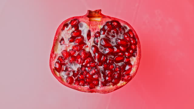 SLO MO LD Half of a pomegranate rotating on a light red surface