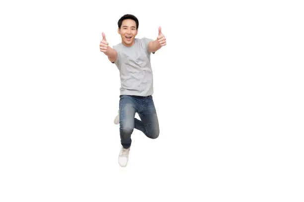 Young Asian man jumping and showing thumbs up isolated on white background