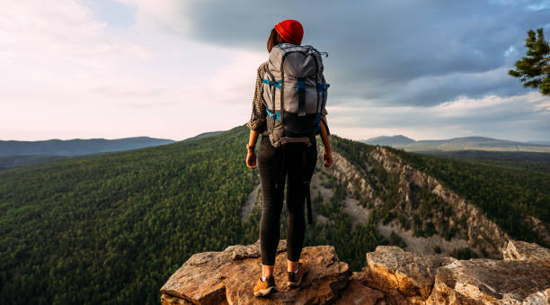 A traveler with a backpack in the mountains at sunset. A traveler with a backpack on the background of mountains, rear view. Hiking trips. A tourist girl on the background of a mountain landscape stock photo