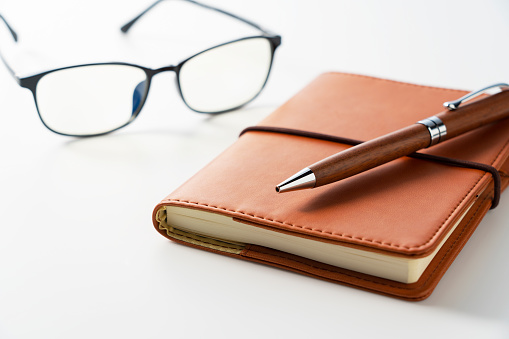 Leather notebook, pen and glasses placed on a white background. Business image.