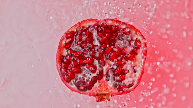 SLO MO LD Half of a pomegranate rotating on a light red surface and water is being sprinkled over it