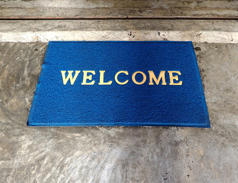 blue doormat with word welcome on cement floor in front of doorstep
