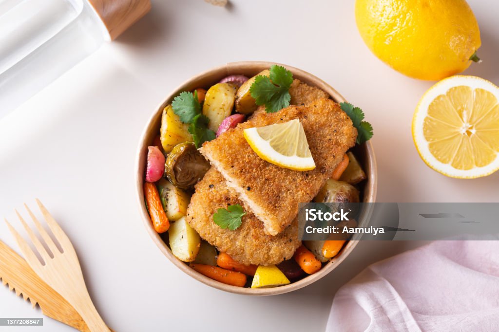 Vegan Plant based fish with crispy batter and roasted vegetables Food to reduce carbon footprint. Vegan Plant based fish with crispy batter and roasted vegetables in a zero waste reusable recycling cardboard packaging Seafood Stock Photo