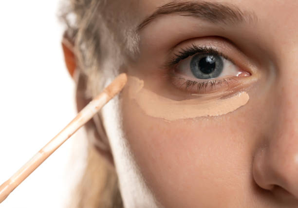 woman applies concealer under her eye closeup of a young beautiful woman applies concealer under her eye on a white background concealer stock pictures, royalty-free photos & images