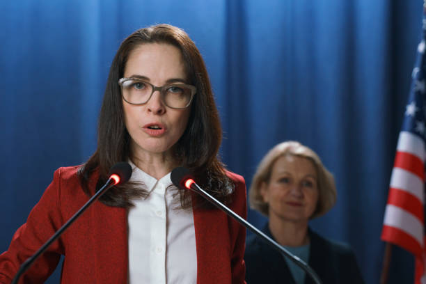 Female American politician gives a serious speech at the debates on a blue background, Female American politician gives a serious speech at the debates on a blue background, we see a female secretary standing behind her speaker of the house stock pictures, royalty-free photos & images