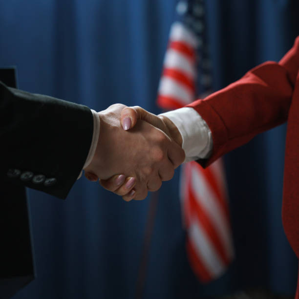 Close-up of a handshake of a man and a woman politicians on a blue background with a US flag Close-up of a handshake of a man and a woman politicians on a blue background with a US flag american propaganda stock pictures, royalty-free photos & images