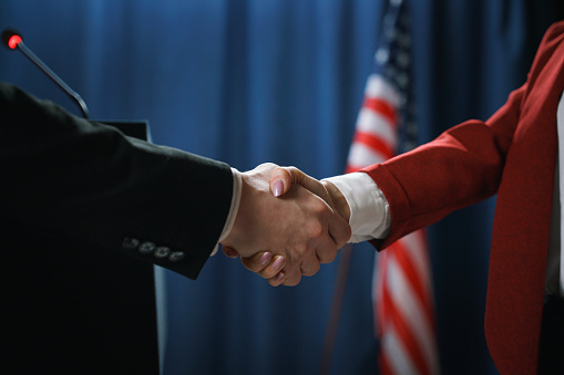 Close-up of a handshake of two politicians after negotiations on a blue background with a US flag