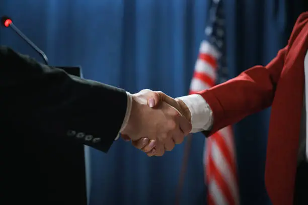 Close-up of a handshake of two politicians after negotiations on a blue background with a US flag