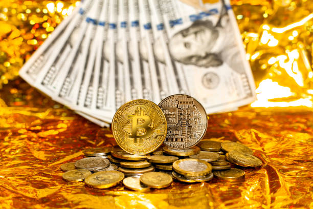 dois bitcoins em uma pilha de moedas contra um fundo de notas de cem dólares dispostas em um ventilador em um fundo dourado - beak number 100 hundred dollar - fotografias e filmes do acervo