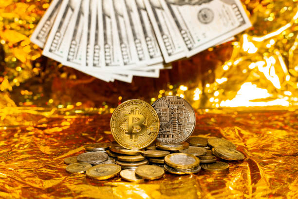 dois bitcoins em uma pilha de moedas contra um fundo de notas de cem dólares dispostas em um ventilador em um fundo dourado - beak number 100 hundred dollar - fotografias e filmes do acervo