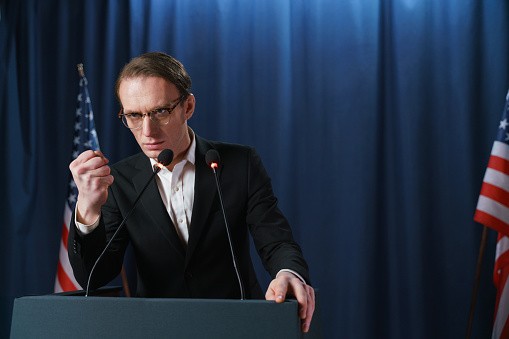 Public speaker stands behind a microphone and makes a statement at a public event or press conference