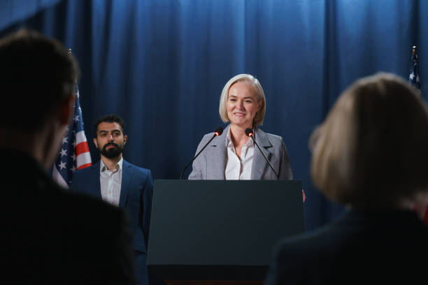 smiling blond female politician gives a speech at the debates, we see the audience in the foreground - press conference public speaker politician speech imagens e fotografias de stock