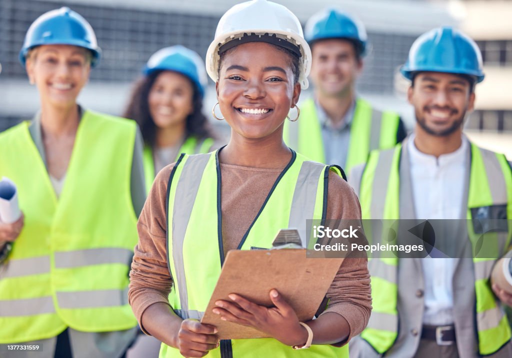 Cropped portrait of an attractive female construction worker standing on a building site with her colleagues in the background We've got all bases covered Construction Industry Stock Photo