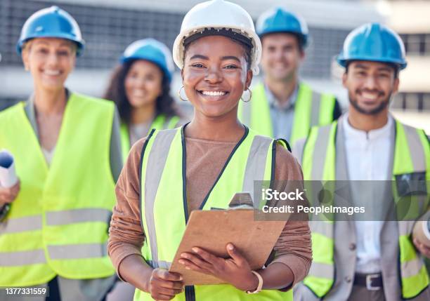 Cropped Portrait Of An Attractive Female Construction Worker Standing On A Building Site With Her Colleagues In The Background Stock Photo - Download Image Now