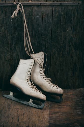 Seasonal winter holiday scene with pair of white ice skates on rustic wooden background with copyspace.