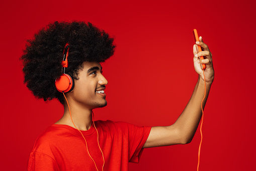 Attractive young adult woman in red clothes listening to the music touching big headphones with closed eyes isolated on white background
