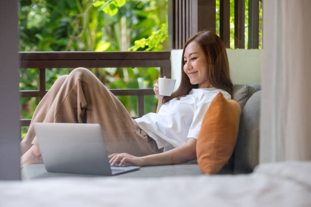 istock Portrait image of a young woman using laptop computer for working or studying online while drinking coffee and laying on sofa at home 1377374983