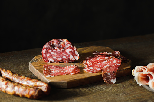 Thinly sliced salami on a wooden cutting board. Close-up of sliced salami on kitchen counter with breadsticks.