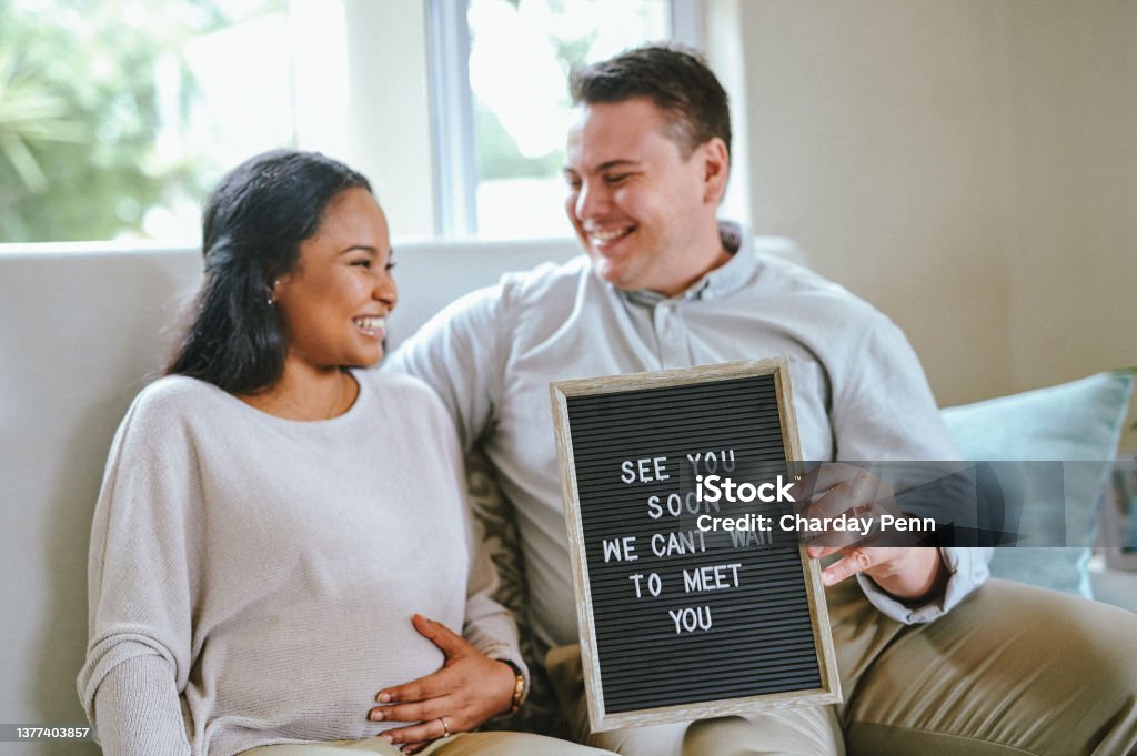 Shot of a couple holding a sign inside a house I love babies Pregnant Stock Photo
