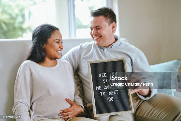 Shot Of A Couple Holding A Sign Inside A House Stock Photo - Download Image Now - Pregnant, Single Word, Morning
