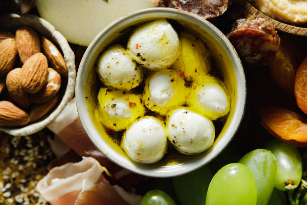 Close-up of mozzarella cheese balls bowl with almonds, dried apricots, prosciutto, green grapes around.  Top view of charcuterie board of assorted food.