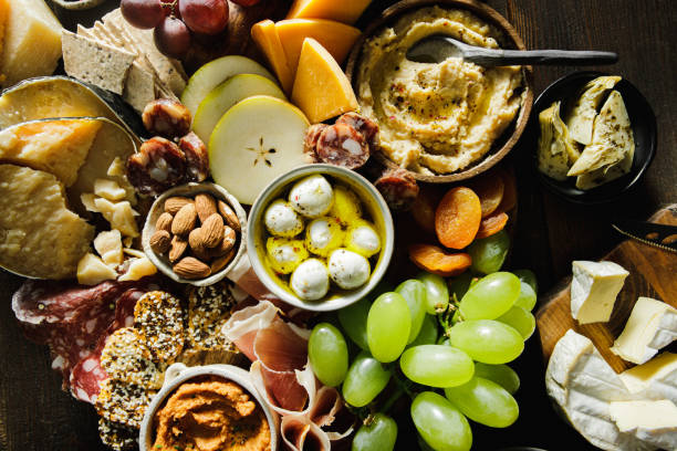 Cheese and meat platter on table Top view of large variety of food on table. Charcuterie board of assorted meats, cheeses, fruits and appetizers. artichoke diet stock pictures, royalty-free photos & images