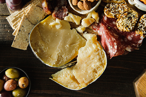 Close-up of parmesan cheese with crakers, thin meat slices, on table. Cheese and meat platter on wooden table.