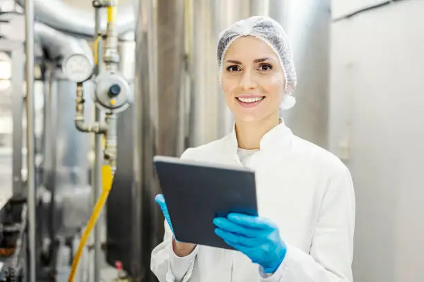 A female milk plant supervisor scrolling on tablet and smiling at the camera.