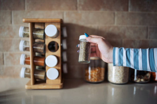 Cropped hand holding jar of spices on kitchen counter. stock photo