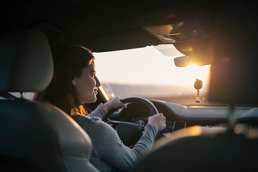Young woman driving car during sunset.