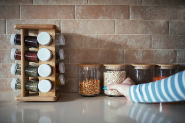 Cropped hand holding jar of spices on kitchen counter. Cropped hand holding jar of spices on kitchen counter. spice rack stock pictures, royalty-free photos & images