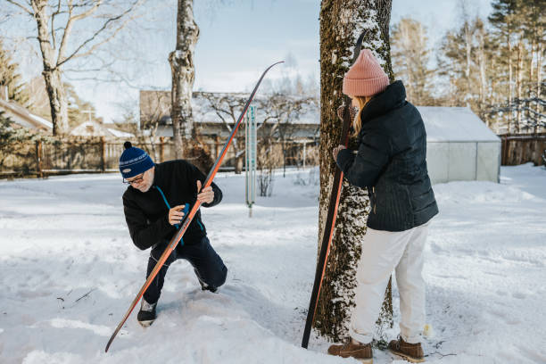 Senior father and adult daughter preparing and waxing skis for day in the nature.