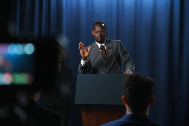 istock Young serious African-American speaker in a gray suit gesturing during his speech at the debates with a shooting camera in the foreground 1377425191