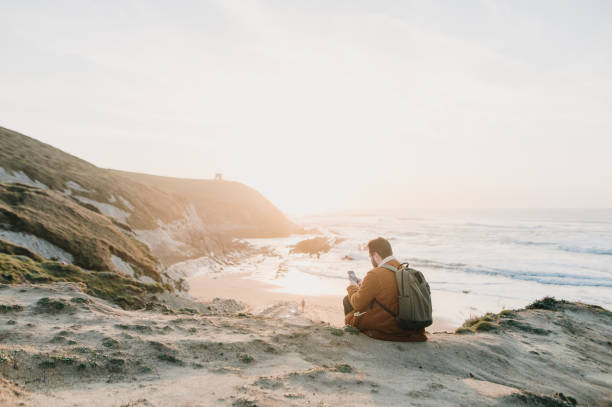 istock Young man sitting by a beach at sunset 1377434558