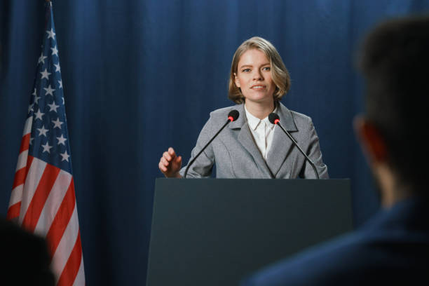 a young pleasant female politician during the speech at the debates standing on a blue background - press conference public speaker politician speech imagens e fotografias de stock