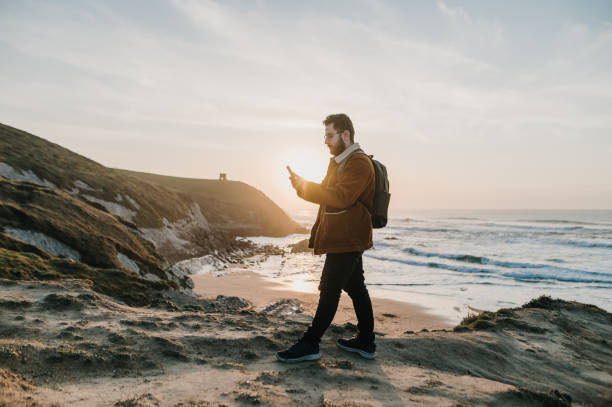 istock Hiker walking by a beach at sunset and using a smart phone 1377435141