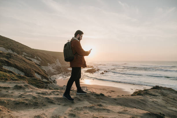 istock Hiker walking by a beach at sunset and using a smart phone 1377435166