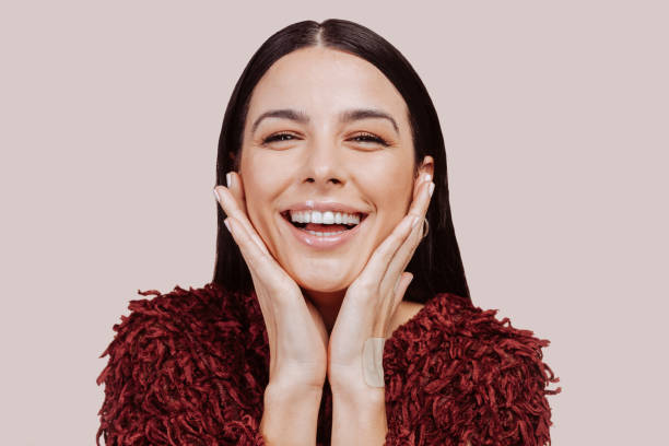 istock Young beautiful happy woman looks in camera at studio with hands on cheek 1377452576