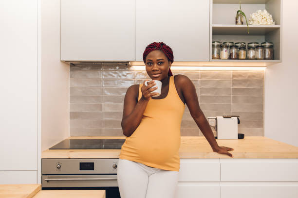 pregnant woman taking a cup of coffee at the kitchen stock photo