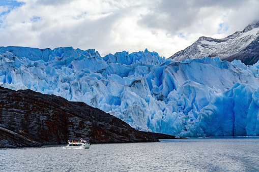 Gray Glacier is a blue glacier in Patagonia, Chile. Great Ice of Gray. Boat with tourists floats among icebergs. Huge iceberg has broken off from the Gray Glacier and drifts across the lake.