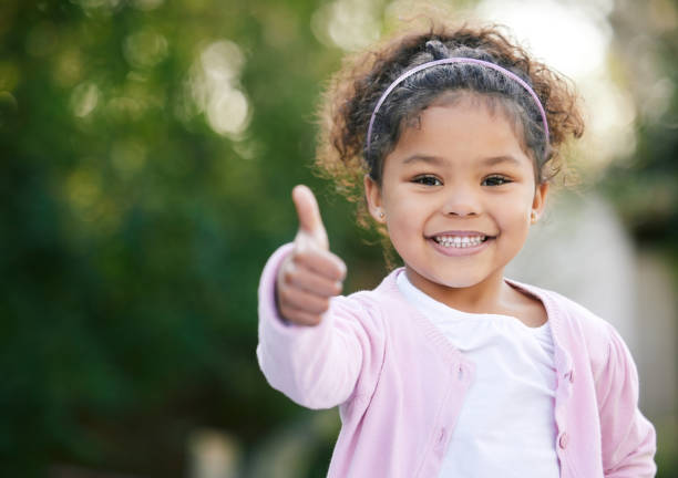 retrato de una adorable niña que muestra el pulgar hacia arriba al aire libre - una sola niña fotos fotografías e imágenes de stock