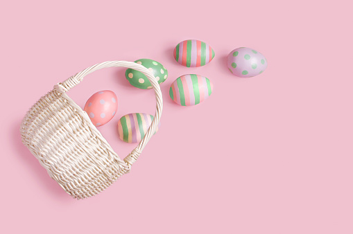a wicker basket lies on a pink background and Easter eggs near it, Easter. High quality photo