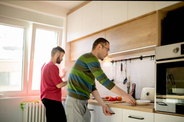 istock Young man with eyeglasses taking plates out, preparing lunch with his partner 1377553757