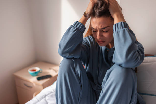 Anxious woman crying in bed Anxious young woman wearing pajamas, sitting on bed in the morning, holding head in hands, crying emotional stress stock pictures, royalty-free photos & images