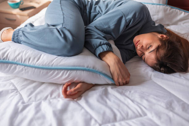 Woman having menstrual cramps lying in bed stock photo