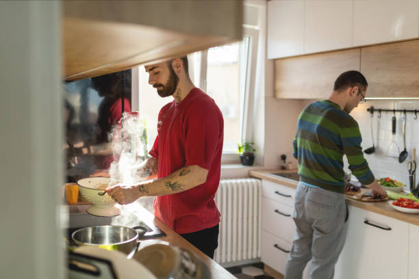 istock Young man holding colander with steaming hot pasta over sink, his partner cutting vegetables 1377558122