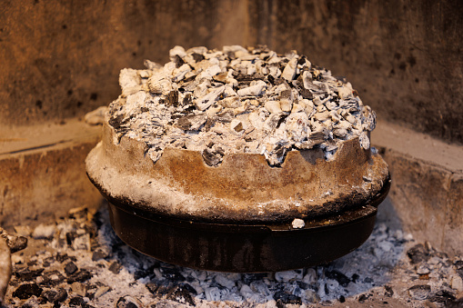 Special cast iron pot for roasting meat under the lid on ember in fireplace, heap of hot ember covering bell lid