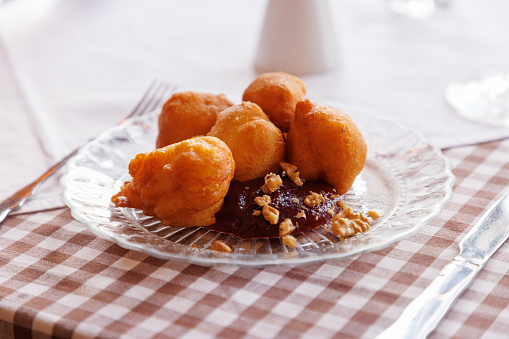Serving size of fritters with plum jam and crushed nuts on top, served traditionally in glass plate on ethnic restaurant table